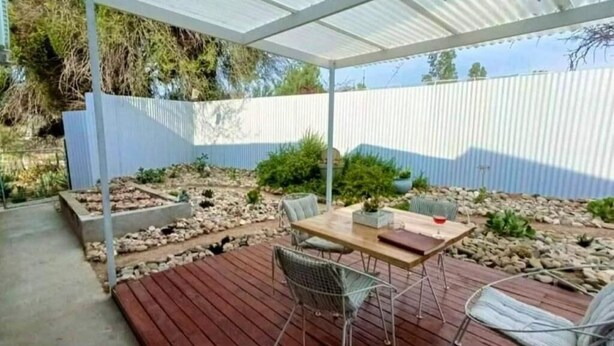 An outdoor patio with a wooden deck, metal chairs, a table, and a covered area. - Karoo Nest Calitzdorp (Calitzdorp)