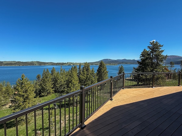 Une terrasse en bois avec une rambarde en métal, donnant sur un lac et des collines boisées.