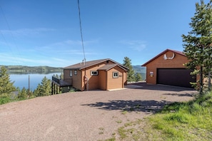 Une cabane à deux étages avec un garage, une terrasse et une vue sur un lac.