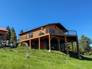 Een houten huis met twee verdiepingen en een balkon, gelegen op een groene heuvel.