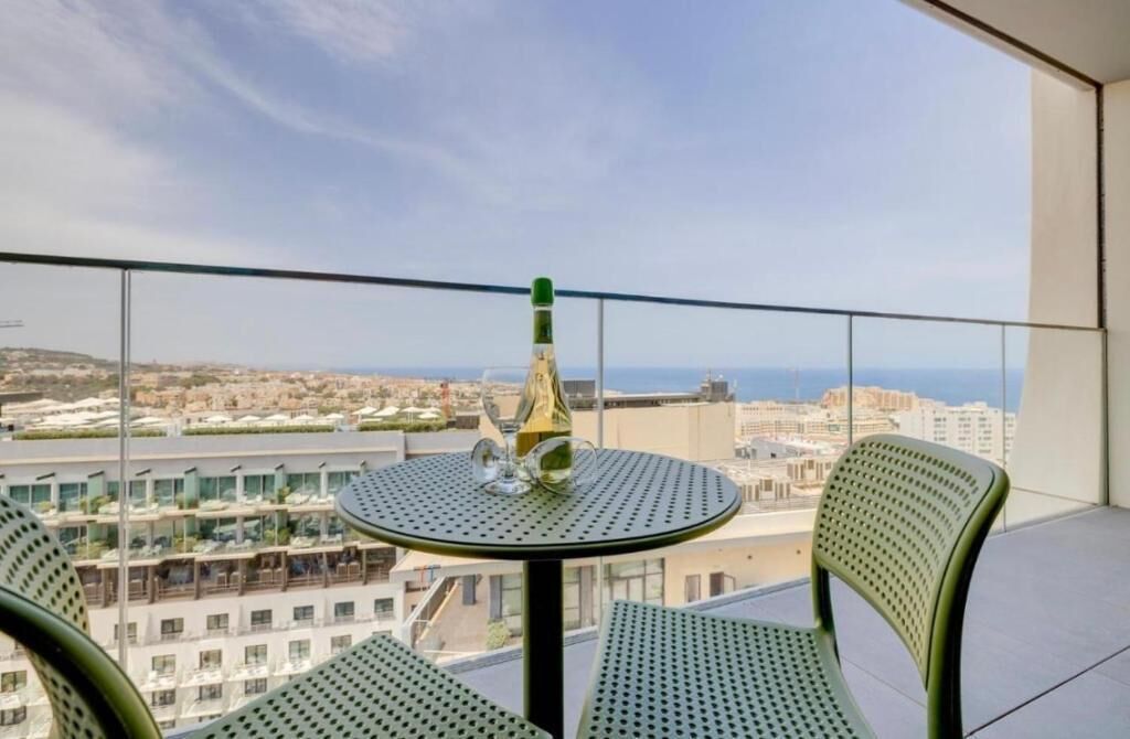 Un balcón con una mesa, sillas, una botella y vistas a un paisaje urbano.