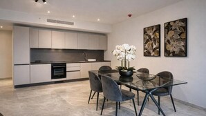 A modern kitchen with grey cabinets, a black countertop, and a dining area with a glass table and grey chairs. - Mercury tower suites by Asignatures (St. Julian's)