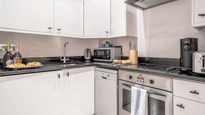 Uma cozinha moderna com armários brancos, lava-louças Bosch, micro-ondas, cafeteira e torradeira.