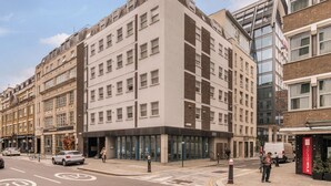 Un edificio de varios pisos con un diseño arquitectónico moderno, que cuenta con una entrada a nivel de calle con puertas de vidrio y una escalera visible que conduce a los pisos superiores.
