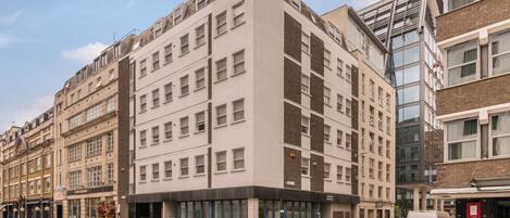 Ein mehrstöckiges Gebäude mit moderner Architektur, mit einem Eingangsbereich auf Straßenniveau, der Glastüren und eine sichtbare Treppe zu den oberen Stockwerken aufweist.