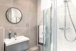 A modern bathroom with a glass shower enclosure, a round mirror, and a white sink. - Kula London Tower Bridge (London)