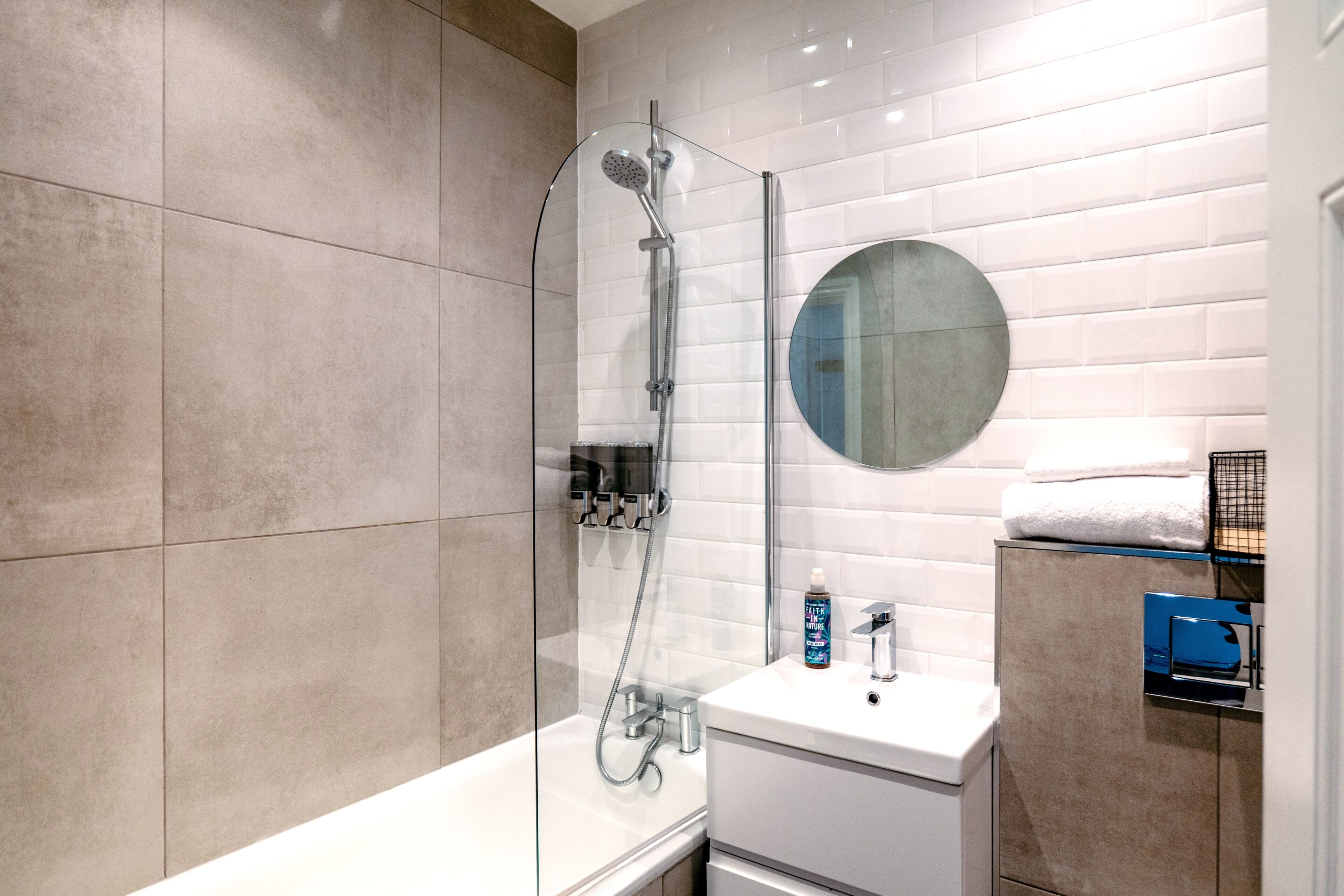 A modern bathroom with a glass-enclosed shower, a round mirror, and a white sink.