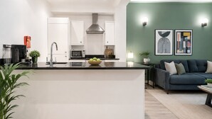 Una cocina moderna con armarios blancos, una isla central y un área de comedor con un sofá oscuro y una mesa de centro.
