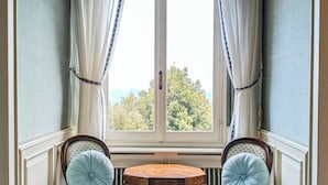 Habitación de esquina con ventanal saliente, dos sillones tapizados con cojines redondos, una mesita redonda y un radiador debajo de la ventana.