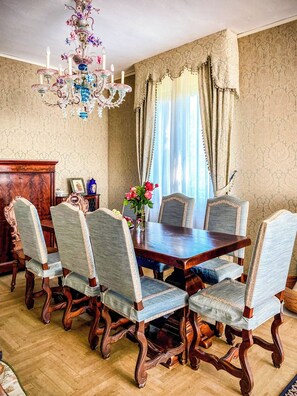Comedor con una mesa de madera, seis sillas tapizadas, una araña y un papel tapiz estampado.