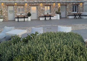 A stone building with outdoor seating, including sofas and a table, and a well-maintained garden area. - Aegean View Apartments (Ornos)