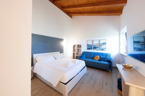 A modern bedroom with a bed, a blue sofa, a wooden ceiling, and a large window. - New Farmhouse TENUTA MARELLA immersed in the Green at the gates of Rome (Lazio)