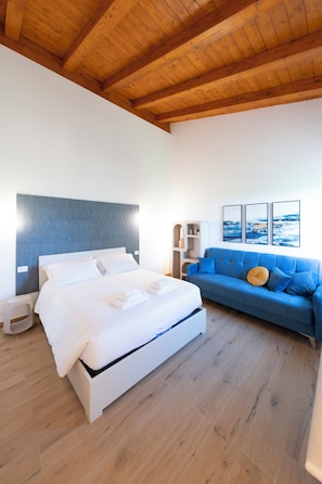 A bedroom with a bed, a blue sofa, and a wooden ceiling. - New Farmhouse TENUTA MARELLA immersed in the Green at the gates of Rome (Lazio)