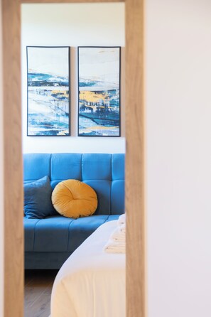 Habitació amb un sofà blau, un coixí groc i dos quadres abstractes emmarcades a la paret.