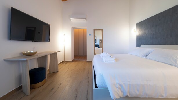 A hotel room with a bed, a flat-screen TV, a bedside table, a mirror, and a wooden ceiling. - New Farmhouse TENUTA MARELLA immersed in the Green at the gates of Rome (Lazio)