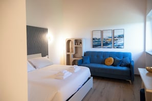 A bedroom with a bed, a blue sofa, a wall-mounted shelf, and two framed pictures. - New Farmhouse TENUTA MARELLA immersed in the Green at the gates of Rome (Lazio)