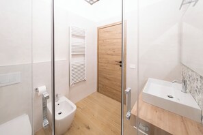 Ein modernes Badezimmer mit einer Duschkabine aus Glas, einer Holztür, einem weißen Waschbecken und einem Bidet.