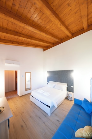 A bedroom with a wooden ceiling, a bed with white bedding, a blue sofa, and a small bedside table. - New Farmhouse TENUTA MARELLA immersed in the Green at the gates of Rome (Lazio)