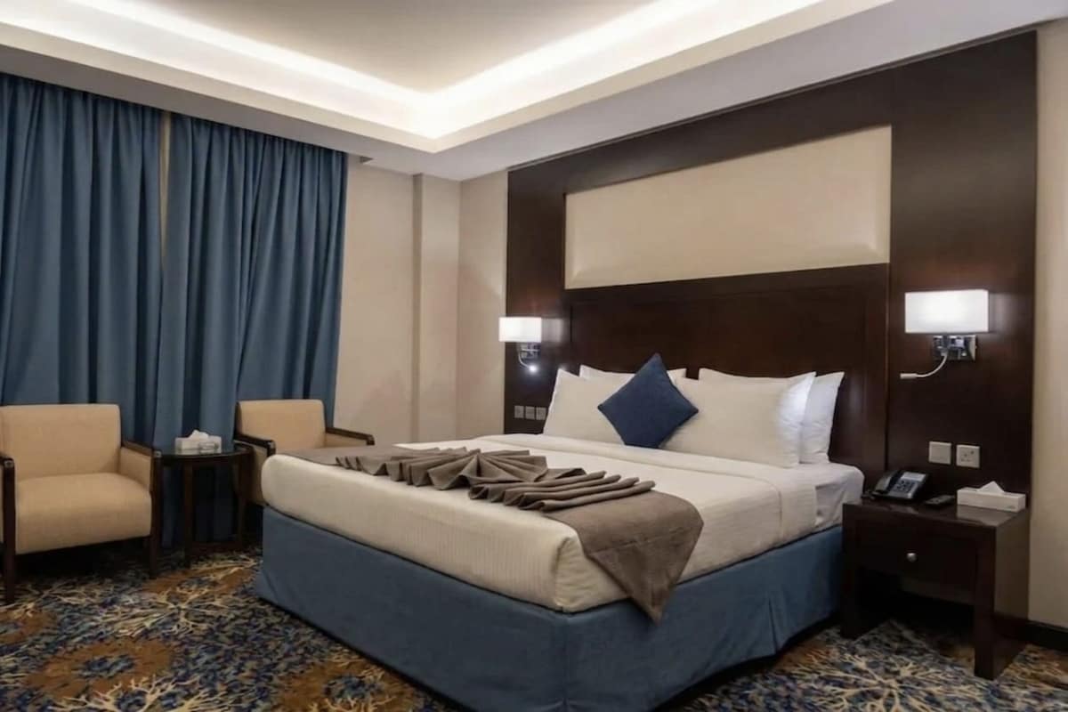Une chambre d’hôtel avec un grand lit, une chaise, une table de chevet et un sol recouvert de moquette.