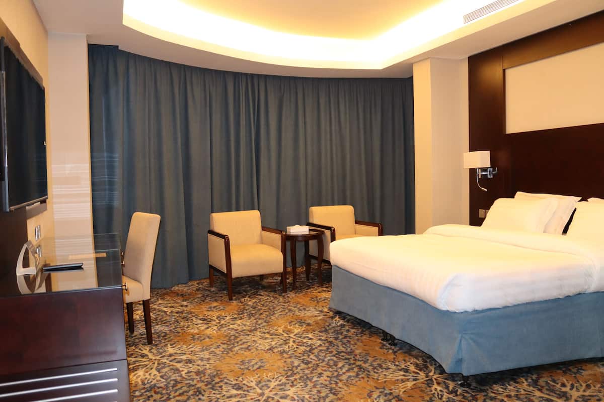 Habitación de hotel con cama, dos sillones, una mesita, televisor y un amplio ventanal con cortinas.