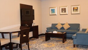 A living room with a sofa, a coffee table, a TV, and framed pictures on the wall. - Vercure Jeddah Alhamra Hotel (Jeddah)