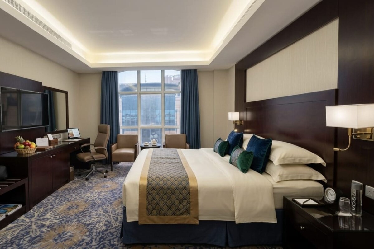 Une chambre d’hôtel avec un grand lit, un bureau avec un ordinateur, une télévision et une fenêtre avec des rideaux.