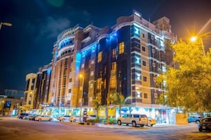 Un hotel de varios pisos con fachada moderna, señalización iluminada y un estacionamiento con varios automóviles.