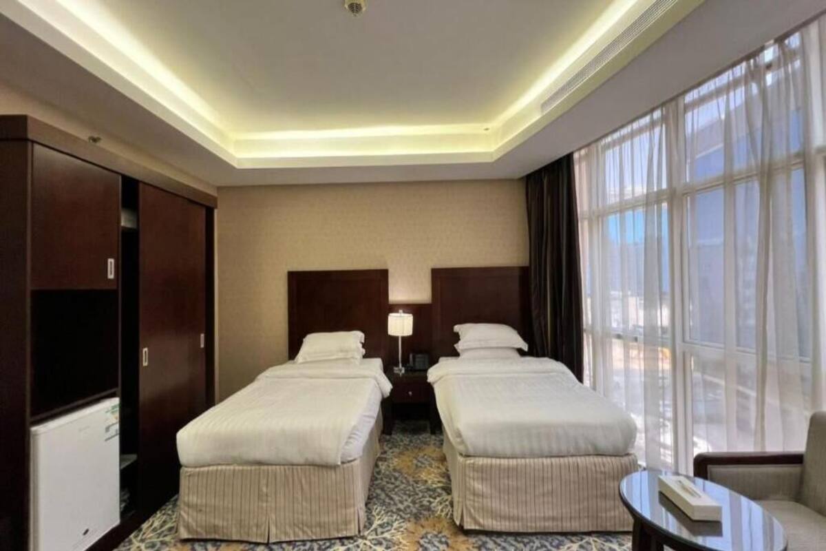 Habitación de hotel con dos camas, un escritorio, una silla, un televisor y un ventanal grande.
