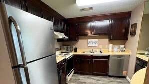 Una cocina compacta con armarios de madera oscura, un refrigerador de acero inoxidable, un microondas y un lavavajillas.