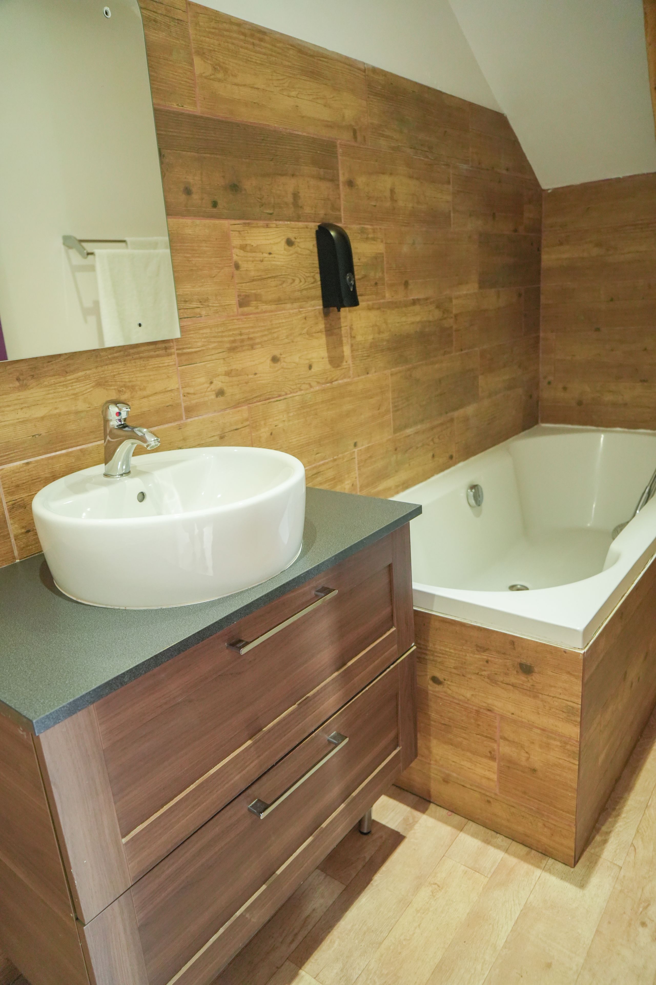 A bathroom with a wooden wall, a white sink, a bathtub, and a mirror.