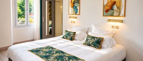 Un dormitorio de hotel con una cama grande, dos lámparas fijadas a la pared y dos cuadros enmarcados con motivos florales.
