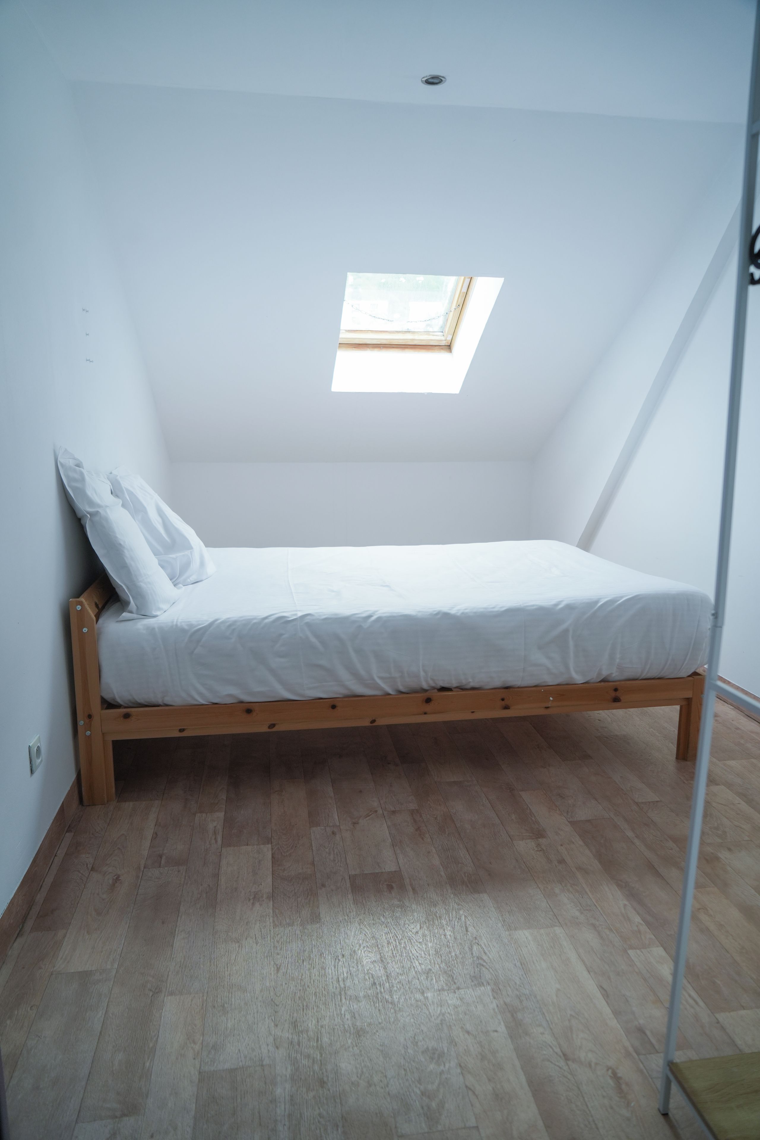 Una habitación pequeña con cama individual, techo inclinado y tragaluz.