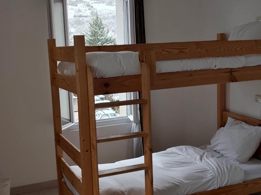 A bunk bed with white bedding, a window with a view of trees, and a door.