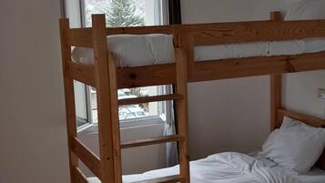 A bunk bed with white bedding, a window with a view of trees, and a door.