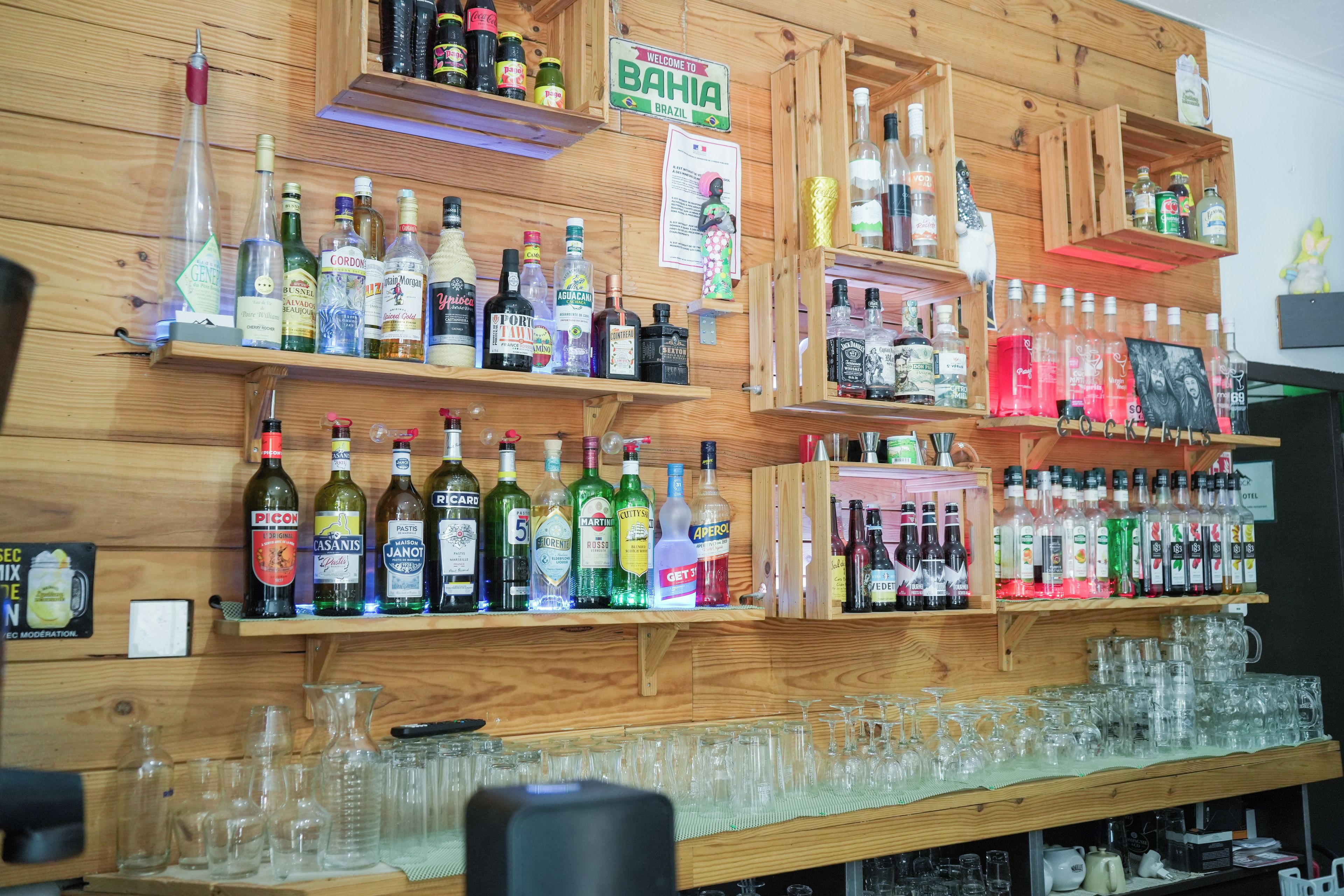 Een bar met planken vol verschillende drankflessen en een selectie glazen.