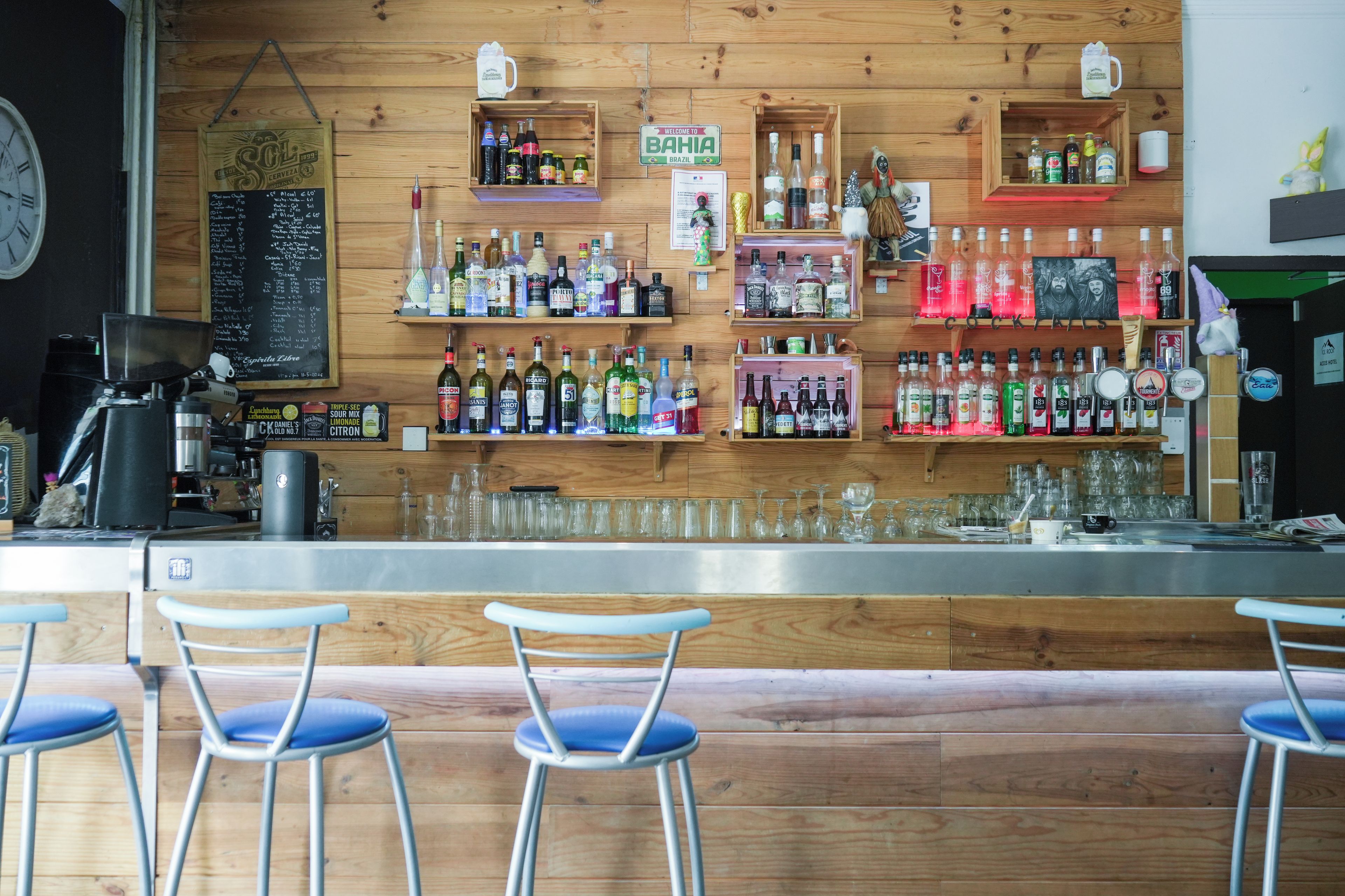A bar area with wooden shelves stocked with various bottles, a coffee machine, and bar stools.