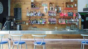 A bar area with wooden shelves stocked with various bottles, a coffee machine, and bar stools.