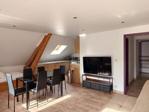 A modern living room with a dining area, a TV, and a loft bedroom with a skylight.