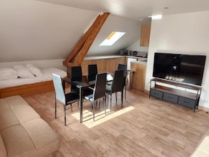 A loft-style room with a dining area, a sofa, a TV, and a kitchen.
