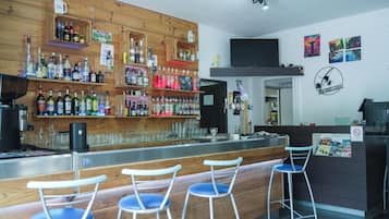 A bar area with wooden shelves stocked with various liquor bottles, a flat-screen TV mounted on the wall, and a bar counter with stools.