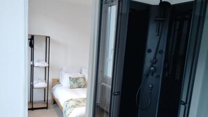 Una habitación con cama, un estante con toallas dobladas y una zona de ducha.