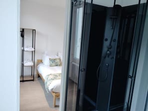 Una habitación con cama, un estante con toallas dobladas y una zona de ducha.