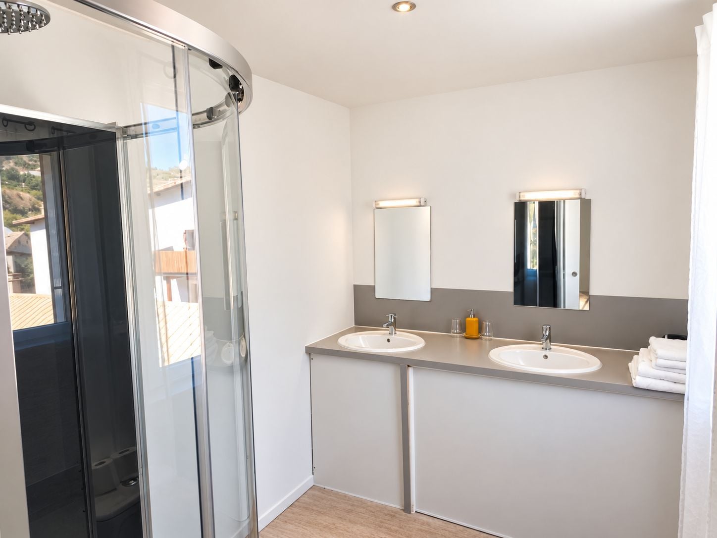 Een moderne badkamer met een douchecabine van glas, twee wastafels en een grote spiegel.