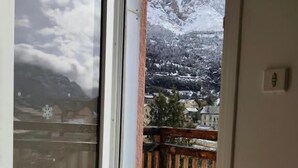 Una habitación con puerta de cristal corredera que da a un balcón con terraza de madera y vistas a montañas nevadas.