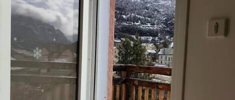 Una habitación con puerta de cristal corredera que da a un balcón con terraza de madera y vistas a montañas nevadas.