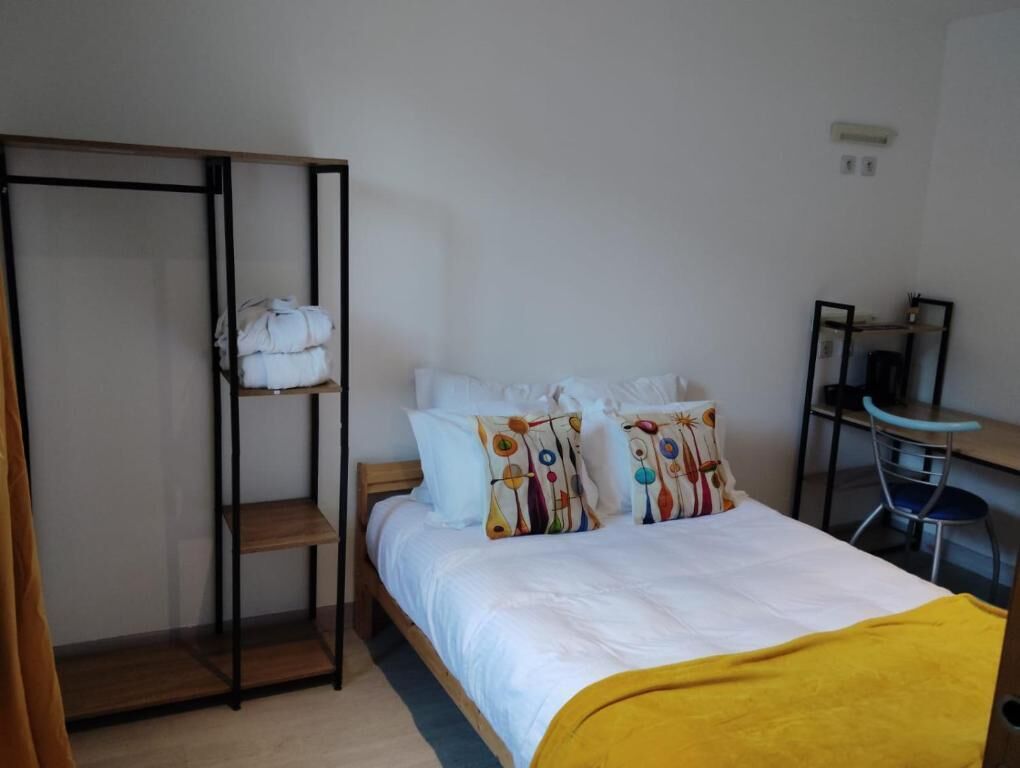 Ein Zimmer mit einem Bett, einem Regal mit gefalteter Kleidung, einem Schreibtisch mit Stuhl und einem Spiegel.