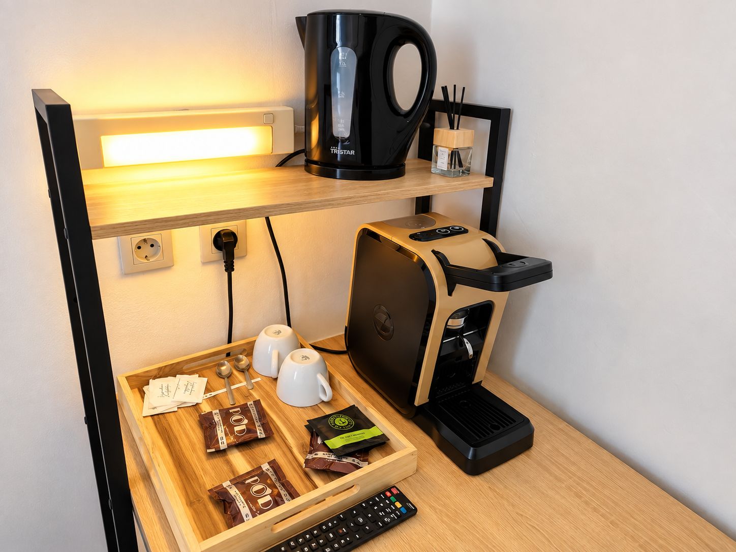 A compact kitchenette with a coffee maker, a kettle, a coffee pod dispenser, and a small refrigerator.
