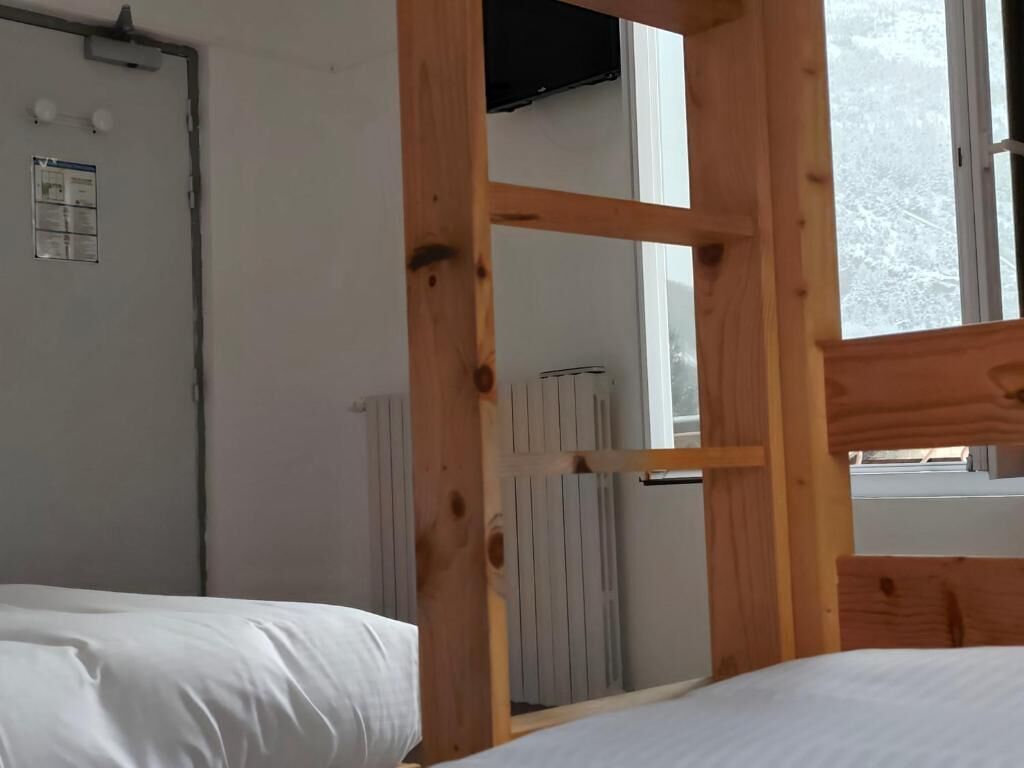Una habitación con estructura de cama de madera, un radiador y una ventana que da a un paisaje nevado.