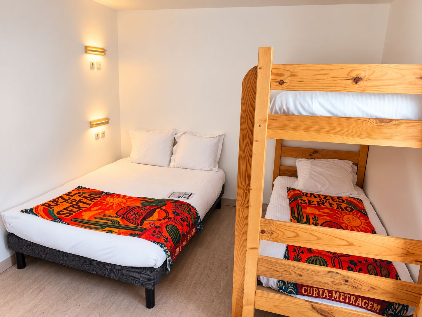 Una habitación con una cama litera y una cama individual, ambas con ropa de cama blanca y una manta colorida en la cama individual.