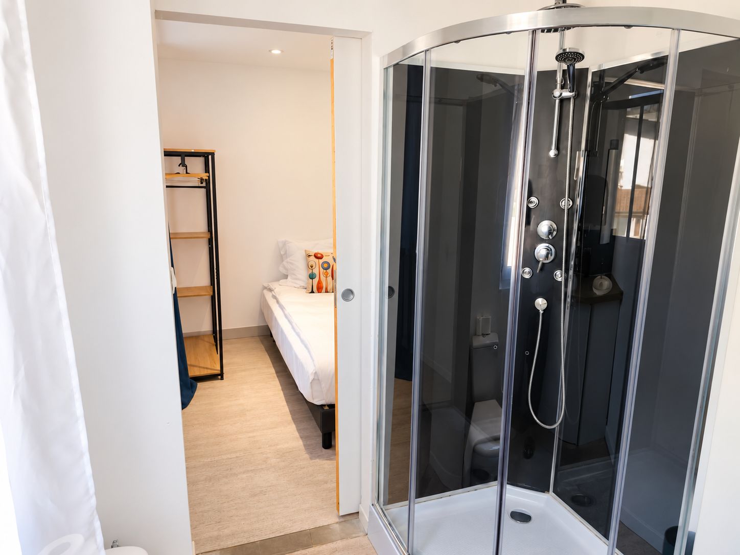 Un baño moderno con ducha de vidrio, una cama con almohada de colores y un estante de madera.